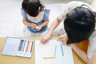 Asyalı anne ve kızı kağıda resim çiziyor.