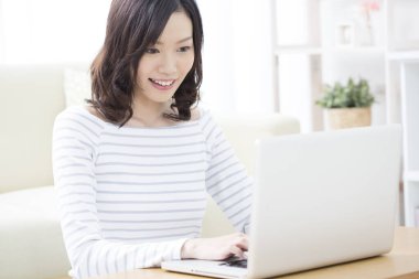 Evde dizüstü bilgisayar kullanan gülümseyen Asyalı kadın.