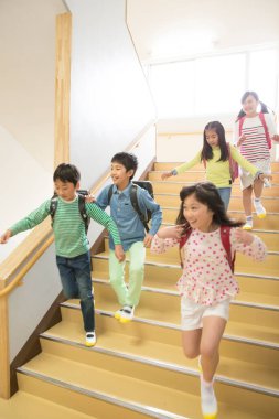 Okulda merdivenlerde koşan sırt çantalı bir grup Japon çocuk.