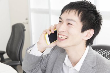 Ofiste telefonla konuşan genç Japon iş adamının yakın plan portresi.