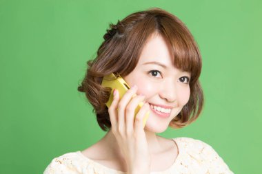 Güzel Japon kadının portresi yeşil arka planda akıllı telefondan konuşuyor. 