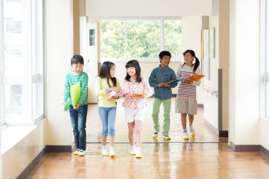 Okul koridorunda yürüyen kitaplarla bir grup Japon çocuk. 