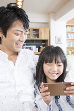 Gülümseyen baba ve kızı evde akıllı telefon kullanıyor.