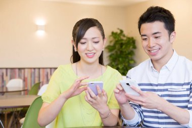 Ofiste akıllı telefon kullanan Asyalı genç ve neşeli bir çift.