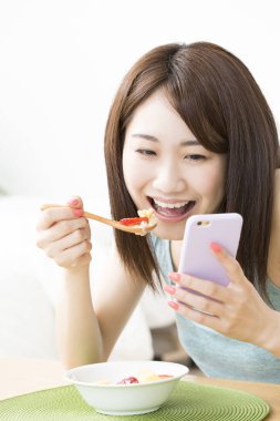 Akıllı telefon beyazı kullanan güzel Asyalı kadın sağlıklı kahvaltı yapıyor.