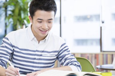 Asyalı öğrenci üniversitede masada okuyor. 