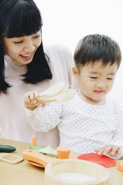Asyalı anne ve oğlu evde tahta oyuncaklarla oynuyorlar. 