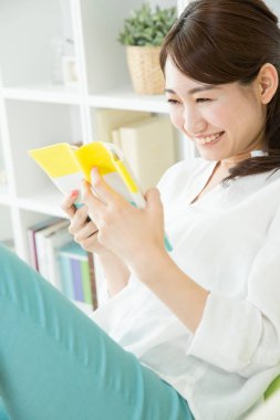 Gülümseyen Asyalı kadın evde kitap okuyor.