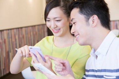 Ofiste akıllı telefon kullanan Asyalı genç ve neşeli bir çift.