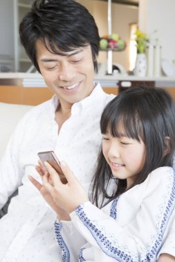 Gülümseyen baba ve kızı evde akıllı telefon kullanıyor.