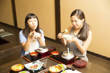 Güzel Asyalı kadınlar restoranda geleneksel Japon yemekleri yiyorlar.