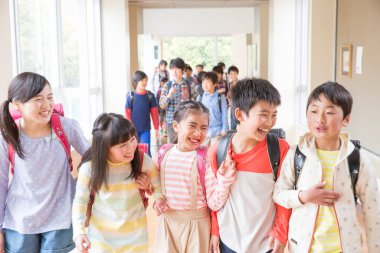 Okul koridorunda sırt çantalı bir grup Japon çocuk yürüyor. 