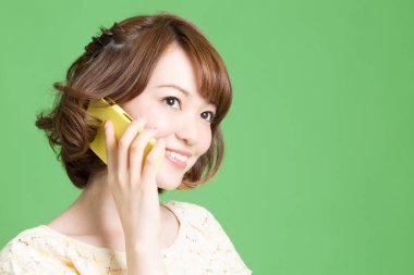 Güzel Japon kadının portresi yeşil arka planda akıllı telefondan konuşuyor. 