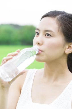 Yeşil yaz parkında gündüz vakti su içen güzel Japon kadın. 