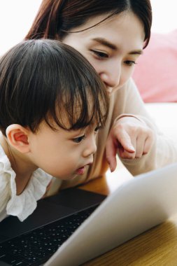 Asyalı anne ve küçük kızı evde dizüstü bilgisayar kullanıyorlar.