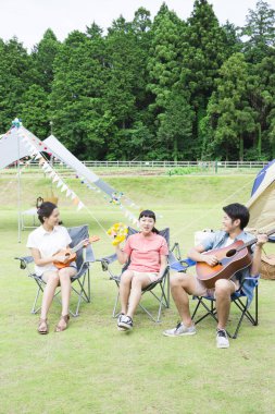 Mutlu Asyalı arkadaşlar kamp parkında müzik aletleri çalıyorlar.