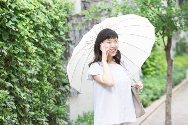 Şemsiyeli genç Asyalı kadın dışarıda akıllı telefondan konuşuyor. 