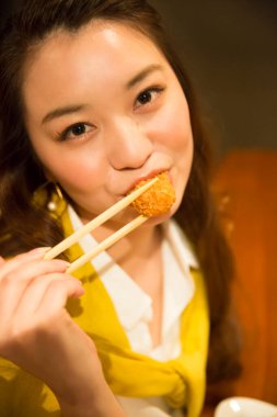 Lokantada yemek çubuklarıyla yemek yiyen kadın.