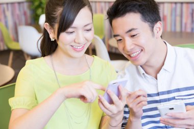 Ofiste akıllı telefon kullanan Asyalı genç ve neşeli bir çift.