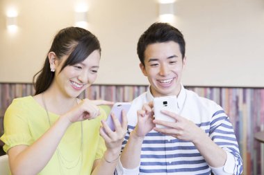 Ofiste akıllı telefon kullanan Asyalı genç ve neşeli bir çift.