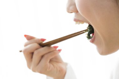 Asyalı kadın evde çubuklarla yemek yiyor.