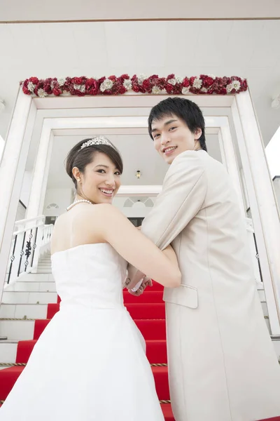 赤いカーペットと階段を歩いて美しい若い結婚式のカップルのバックビュー — ストック写真
