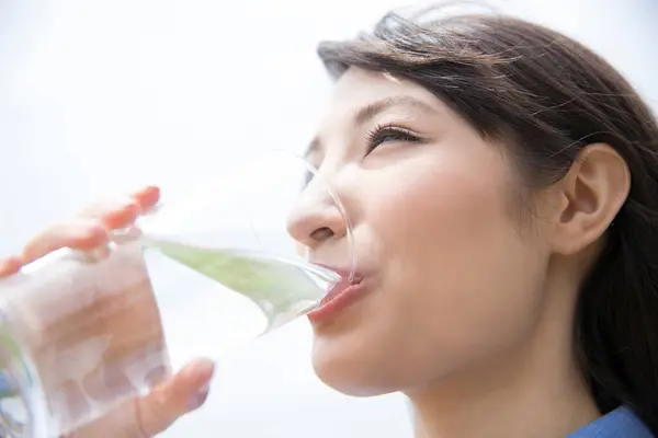 Genç Asyalı kadın açık havada su içiyor.