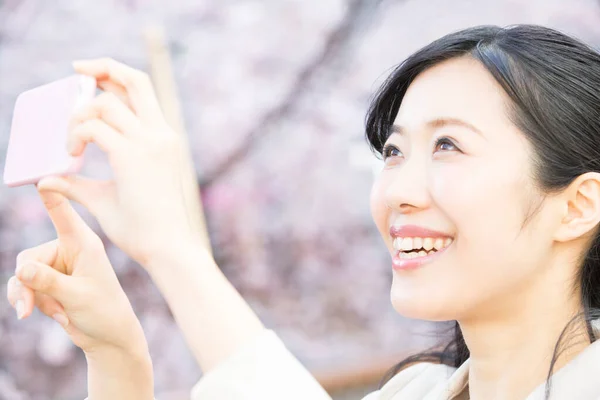 美丽的年轻亚洲女人在春天公园用电话拍照 — 图库照片