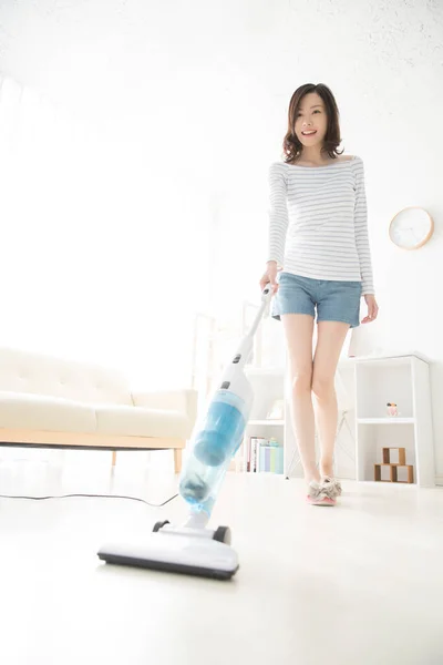 リビングルームの掃除機が付いている若いアジアの女性 — ストック写真
