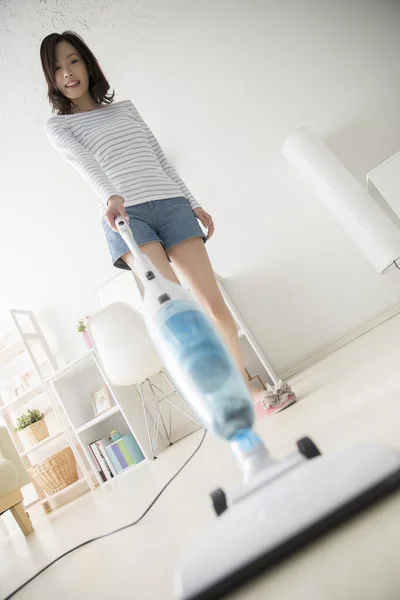 リビングルームの掃除機が付いている若いアジアの女性 — ストック写真