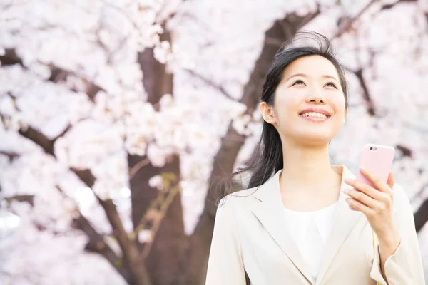 美丽的年轻亚洲女人用智能手机抬头看春天的公园 — 图库照片