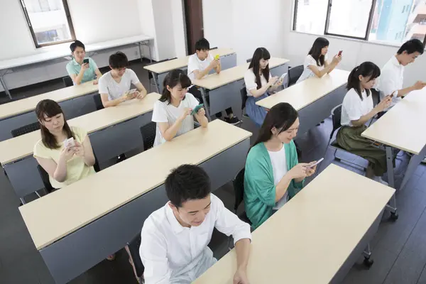 Nuoret Aasialaiset Opiskelijat Käyttävät Älypuhelimia Luokkahuoneessa — kuvapankkivalokuva