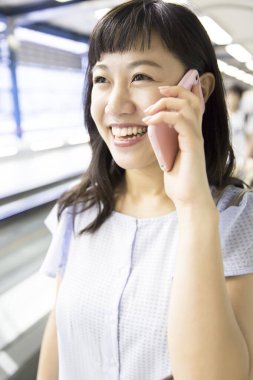 Tren istasyonunda cep telefonu olan genç Asyalı kadın.