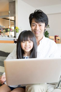 Evde dizüstü bilgisayar kullanan mutlu bir Asyalı aile.