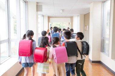 Okul koridorunda sırt çantalı bir grup Japon çocuk yürüyor. Arka plan