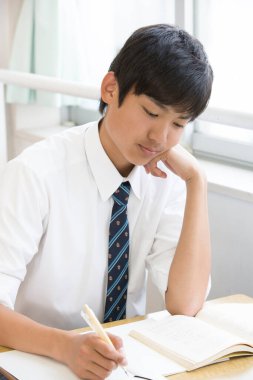 Asyalı öğrenci sınıfta deftere bir şeyler yazıyor.