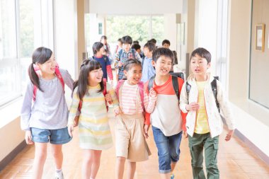 Okul koridorunda sırt çantalı bir grup Japon çocuk yürüyor. 