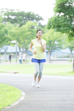 Genç bir kadın parkta koşuyor.