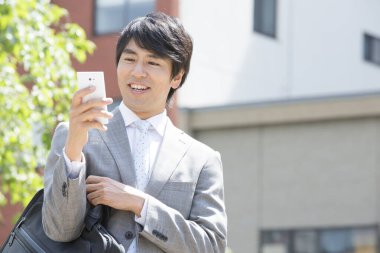 Yakışıklı, gülümseyen Asyalı iş adamı sokakta cep telefonu kullanıyor. 