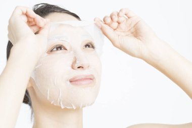 Beyaz arka planda maske takan güzel bir Asyalı kadın. Cilt bakımı kavramı