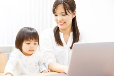 Genç anne ve küçük kızı evde dizüstü bilgisayar kullanıyorlar.