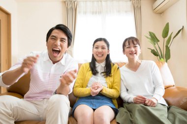  Asyalı bir aile kanepede oturmuş televizyon seyrediyor. 