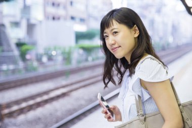 Tren istasyonunda cep telefonu olan genç Asyalı kadın.