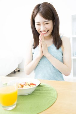 Genç Asyalı kadın mutfakta kahvaltı yapıyor.