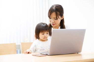 Genç anne ve küçük kızı evde dizüstü bilgisayar kullanıyorlar.