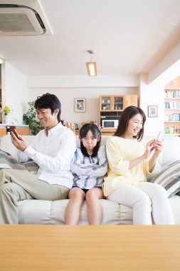 Ailesi kanepede akıllı telefon kullanan üzgün Asyalı kız. 