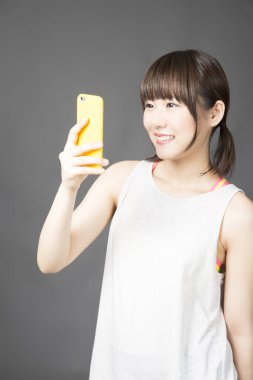 Gri arka planda cep telefonu olan genç Asyalı kadın.