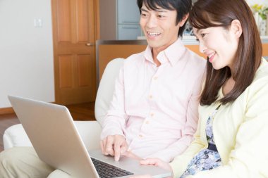 Asyalı çift oturma odasında dizüstü bilgisayar kullanıyor.