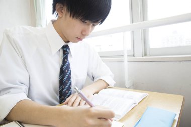 Asyalı öğrenci sınıfta deftere bir şeyler yazıyor.