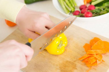 Masada kesme tahtasına taze sarı biber kesen kadın.